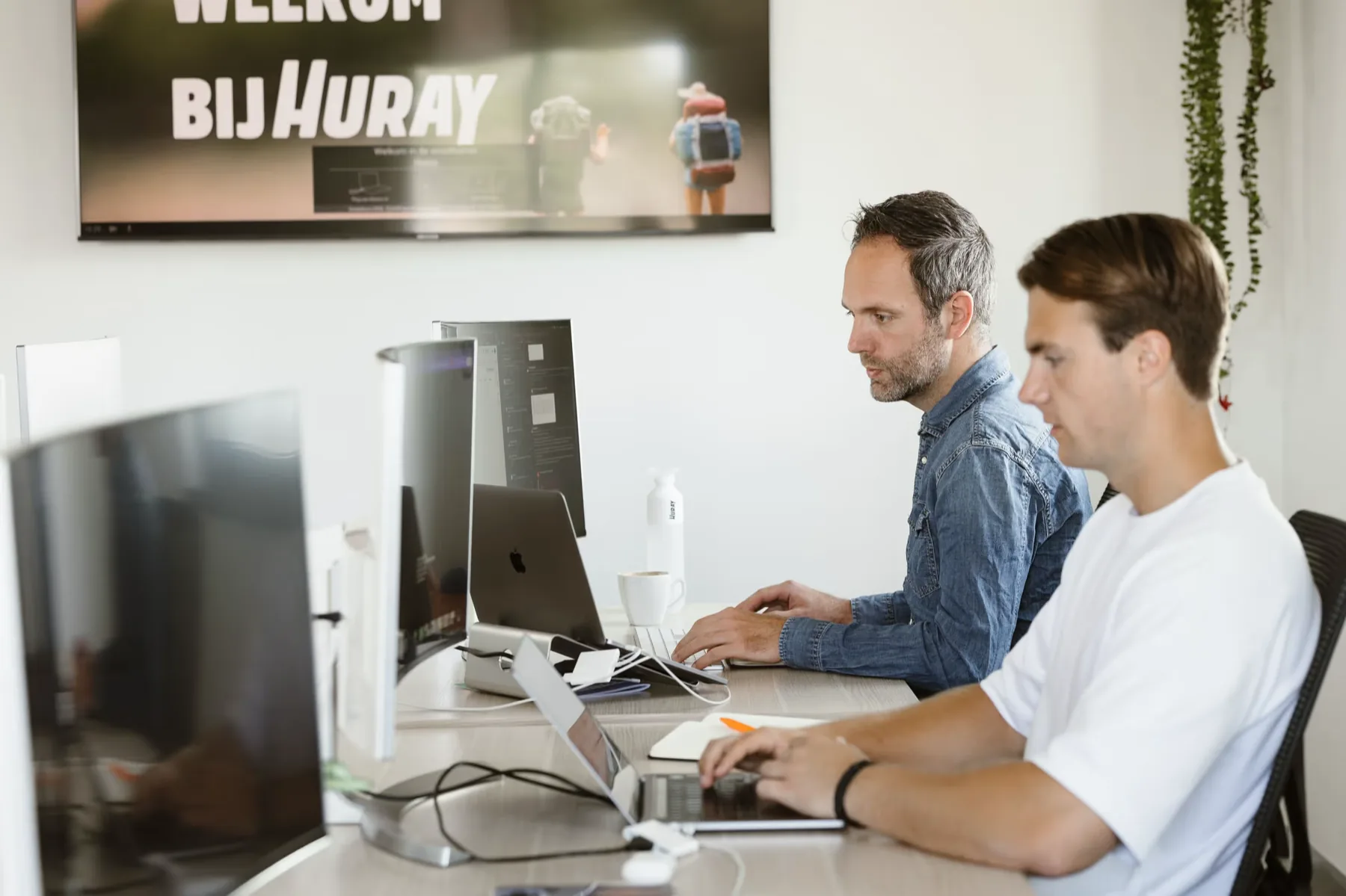 Twee collega's van Huray werken naast elkaar achter hun schermen op kantoor.
