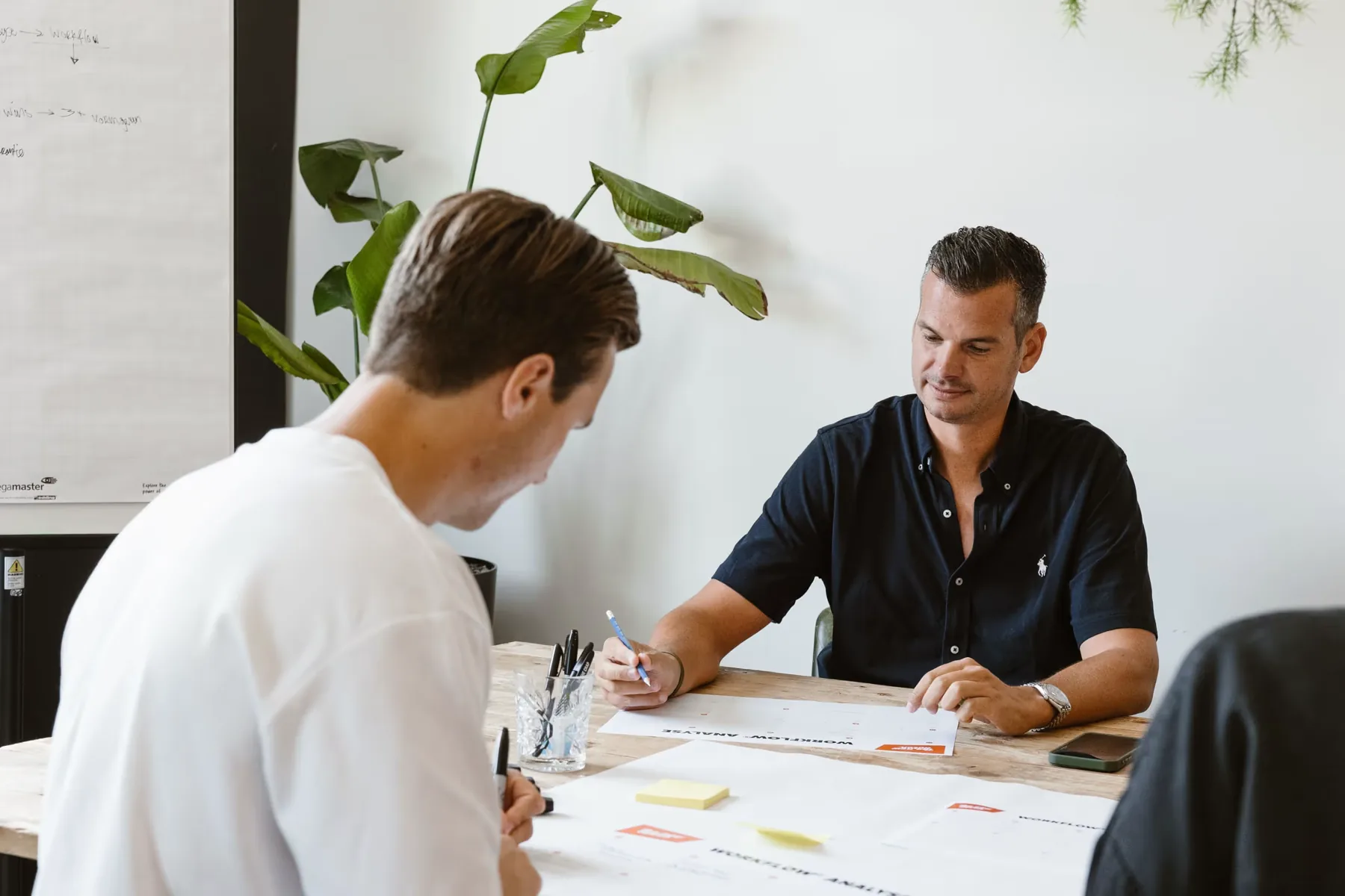 Twee collega's nemen samen aantekeningen en documenten door aan een tafel.